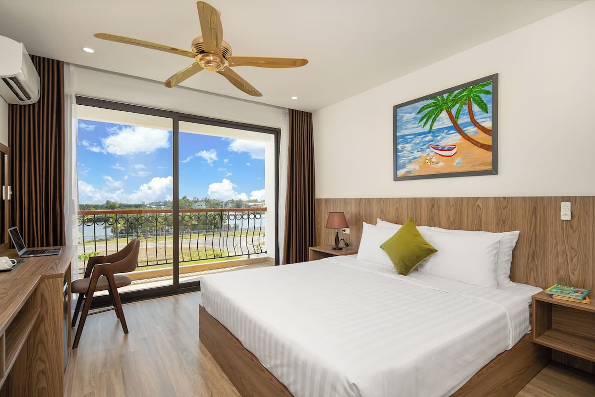 Habitación de hotel con cama, escritorio, silla y un cuadro de una playa.