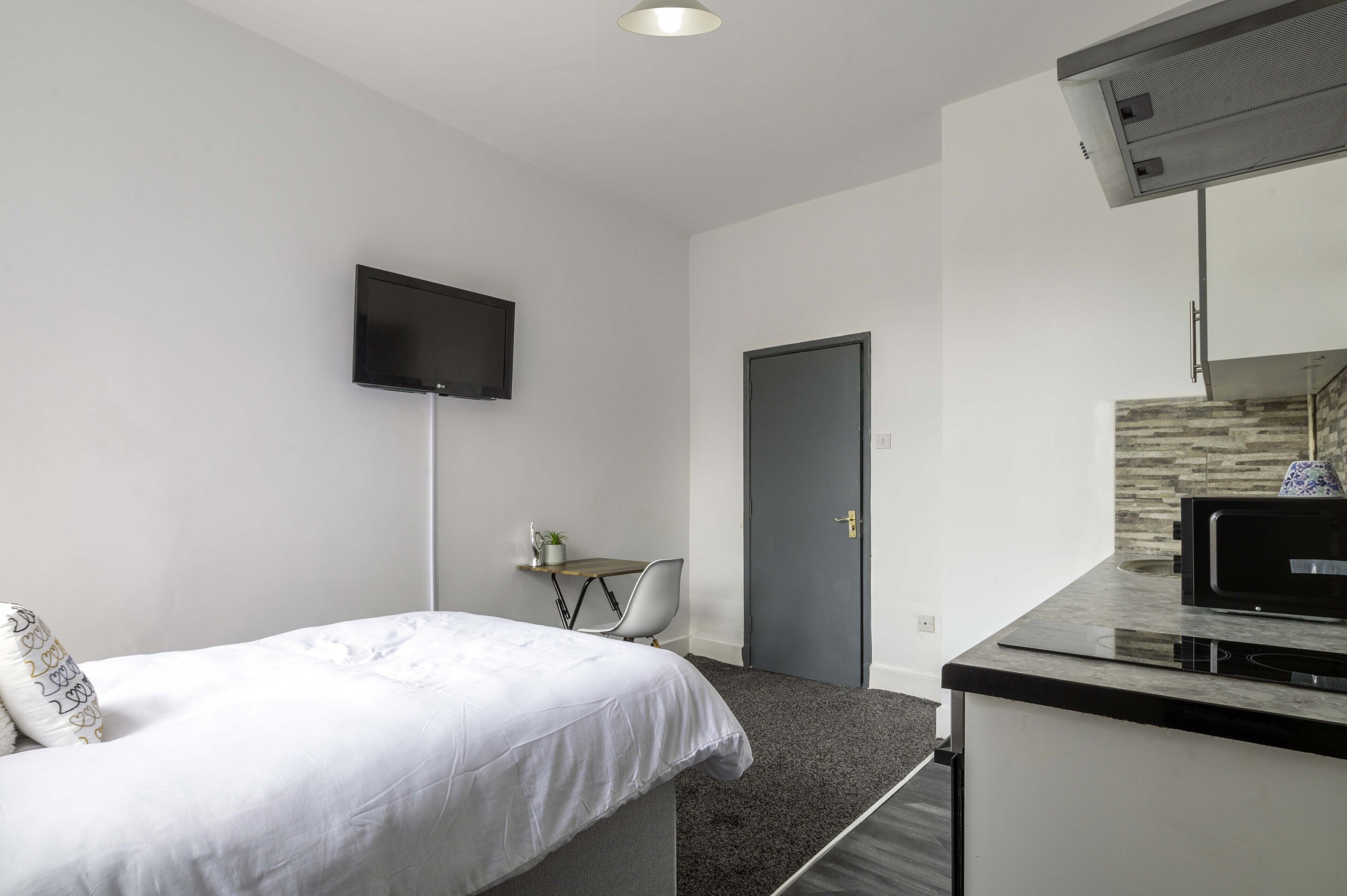 A compact hotel room with a bed, a small desk, a flat-screen TV, a microwave, and a door.