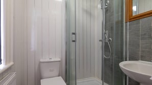 Un baño con inodoro, ducha con mampara de vidrio y lavabo.