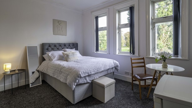 Un dormitorio ordenado con una cama grande, mesitas de noche, una silla y una pequeña mesa con un jarrón.