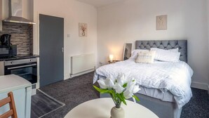 Una habitación de hotel moderna con una cama, una mesita con un florero, una kitchenette y un baño.