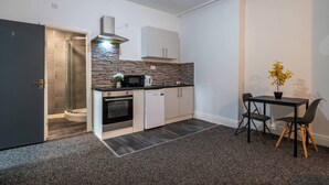 Cocina compacta con horno empotrado, microondas y un refrigerador pequeño. Hay un comedor con una mesa y dos sillas.