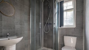 Un baño moderno con ducha envuelta en vidrio, lavamanos blanco y retrete.