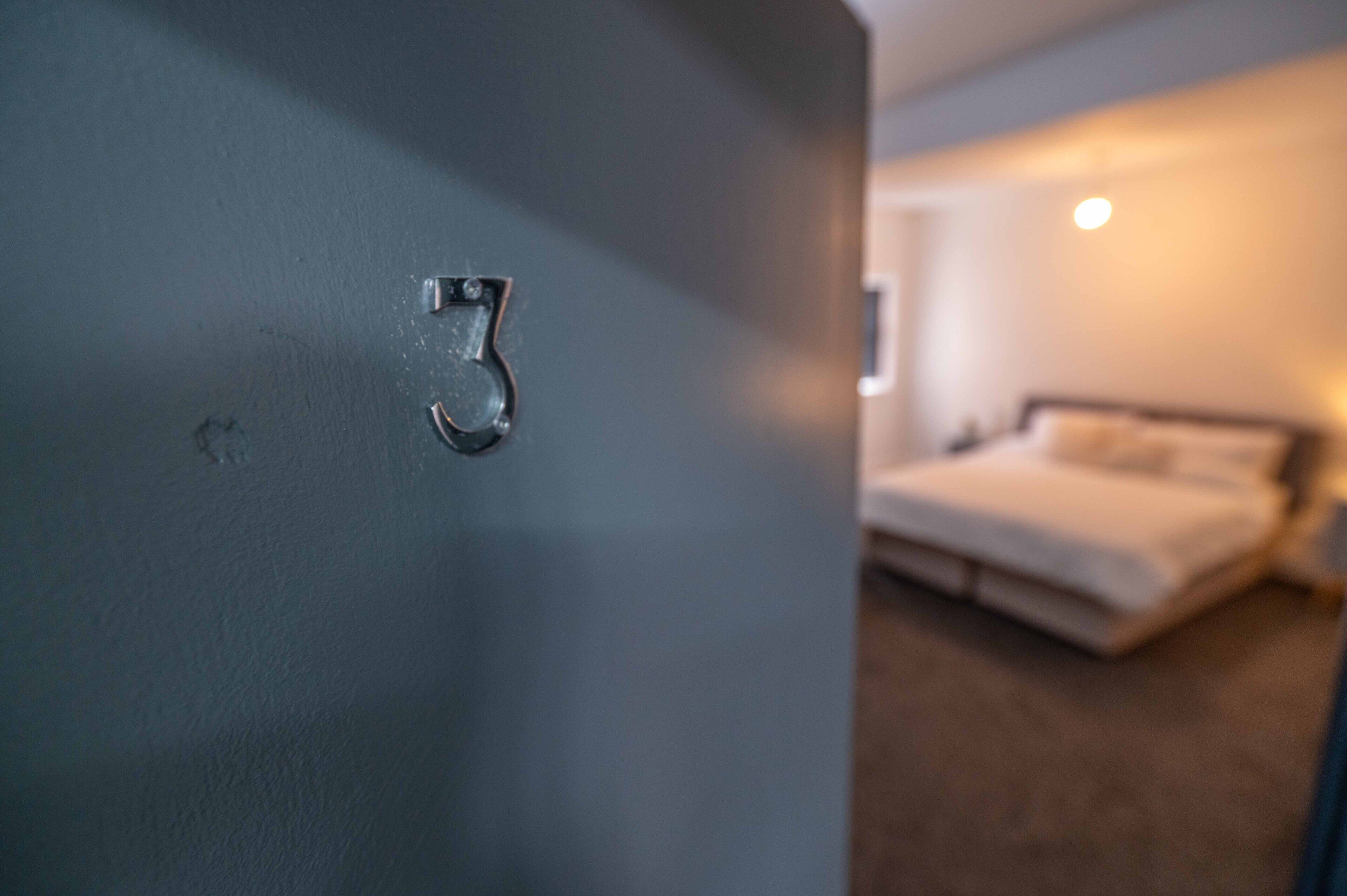 Une porte dotée d’une serrure à trois chiffres, qui donne sur une chambre à coucher comprenant un lit et une table de chevet.