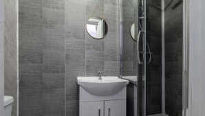 Une salle de bain moderne avec un lavabo blanc, un miroir rond et une cabine de douche en verre.