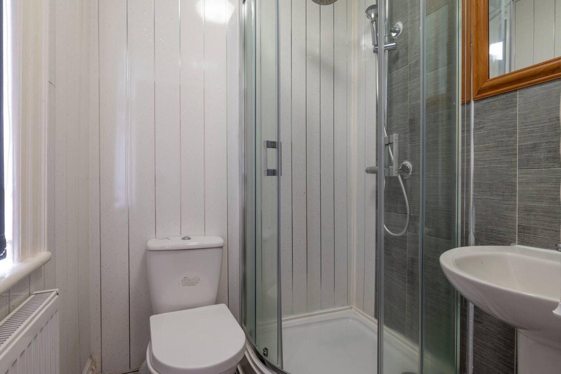 Une salle de bain comprenant des toilettes, une douche fermée par une paroi de verre et un lavabo.
