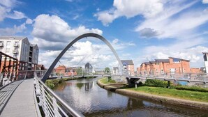 Un pont per a vianants amb una llenca característica sobre un canal, envoltat d'edificis i vegetació.