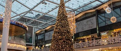Et stort juletræ indendørs i et indkøbscenter med et glaskupl og flere butikker.