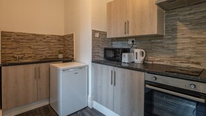 A compact kitchen with wooden cabinets, a built-in microwave, a toaster, and a small refrigerator.