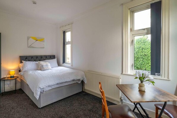 A bedroom with a bed, bedside table, lamp, and a view of greenery through the window. - Fully Serviced 1-bed Studio8 in Coventry (Coventry)