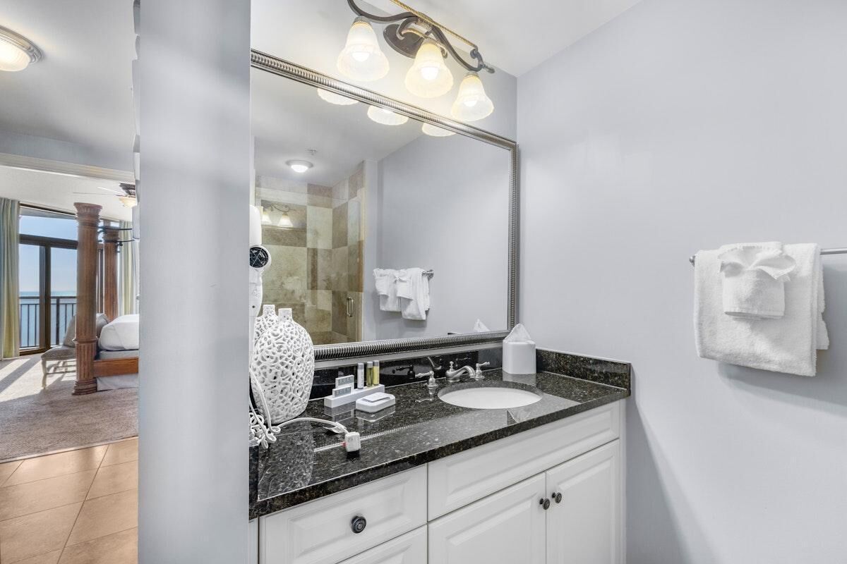 A modern bathroom with a large mirror, granite countertop, and white cabinetry.