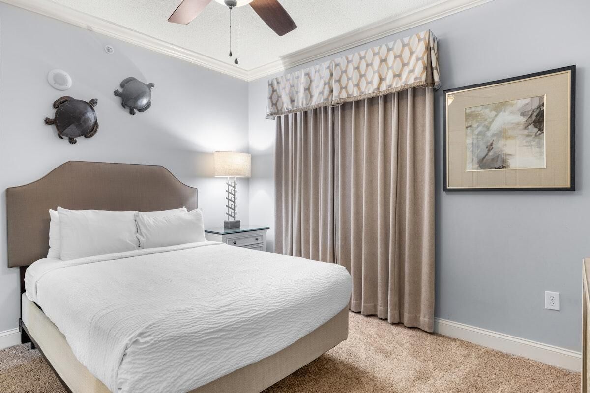 A bedroom with a bed, a nightstand, a lamp, a ceiling fan, and a framed picture on the wall.