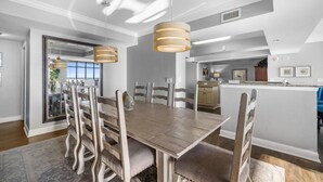 A modern dining area with a wooden table and chairs, pendant lighting, and a view into the kitchen. - Luxurious 5BR Oceanfront Condo at 4-Diamond North Beach Resort & Villas! (North Myrtle Beach)