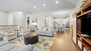 A spacious living room with a grey sofa, white armchairs, and a coffee table. A dining area with a white table and chairs is visible in the background. - Cozy 4 Bedroom Beach House Close to the Ocean (North Myrtle Beach)