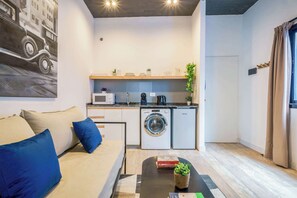 Een knus woongedeelte met een bank, salontafel en een kitchenette, inclusief een magnetron, wasmachine en spoelbak.