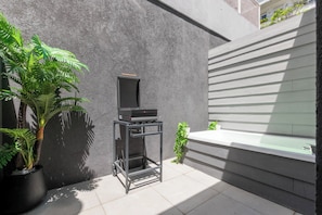 A patio area with a grill, potted plants, and a modern building facade.