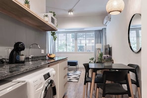 Une cuisine compacte équipée d’un lave-linge, d’une machine à café et d’un coin repas avec une table et des chaises.