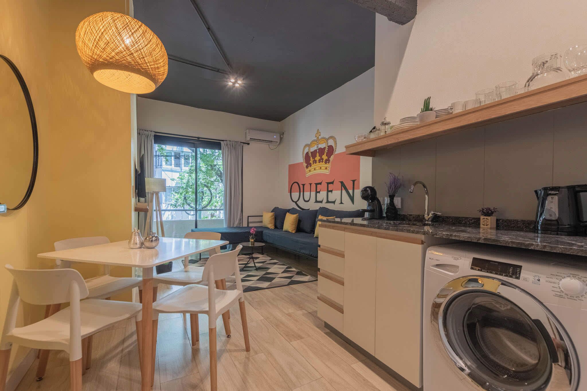 A compact kitchen with a washing machine, a dining area with chairs, and a sofa.