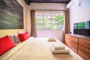 Ein Hotelzimmer mit Bett, Fernseher, Fenster mit Vorhängen und einem Bild an der Wand.