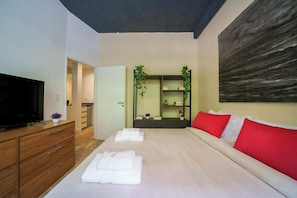 A modern hotel room with a large bed, a flat-screen TV, a wooden dresser, and a small bathroom.