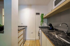 Una cocina compacta con lavadora incorporada, un lavamanos y un microondas sobre una estantería de madera.