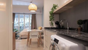 A modern kitchen with a built-in washing machine, a dining area with a table and chairs, and a view of the outdoors through a large window.