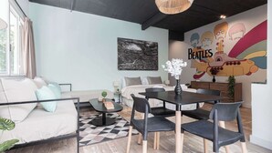 Un salon moderne avec un canapé, une table à manger et des chaises. Un mur est décoré d’une fresque et il y a une fenêtre avec des rideaux.