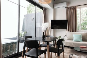 Una sala moderna con sofá, televisor montado en la pared, mesa de comedor con sillas y un ventanal con vistas a la vegetación.