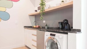 Une cuisine compacte équipée d’un lave-linge, d’une machine à café et d’une étagère contenant des ustensiles de cuisine.