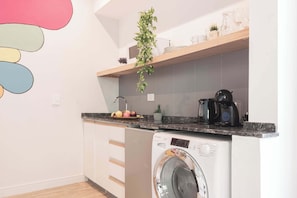 Una cocina compacta con lavadora, cafetera y estante con utensilios de cocina.