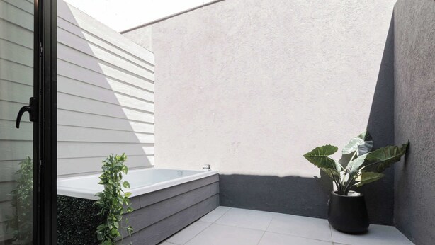 Un petit espace extérieur clos comprenant un jacuzzi, une plante en pot et une porte vitrée.