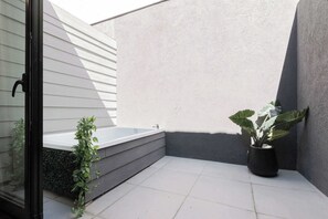 A small, enclosed outdoor area with a hot tub, a potted plant, and a glass door.