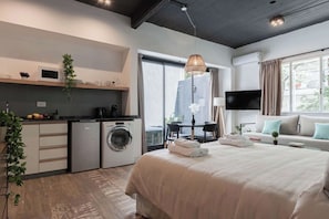 Una habitación de hotel moderna con una cama grande, un comedor, una cocina con microondas y una lavadora.