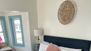 Un letto rifatto con lenzuola bianche e una soffice coperta rosa, un poggiatesta blu scuro e una decorazione murale tessuta.