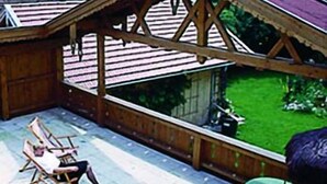 Eine Holzhütte mit geneigtem Dach, einer Terrasse mit Gartenmöbeln und Blick auf eine Berglandschaft.