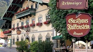 A traditional building with a balcony and flower boxes, labeled "Metzgerei Schwäizer" and "Gasthaus Jallenstein." - Ferienwohnung Typ C ca. 62 qm bis Vier Personen (Flintsbach am Inn)
