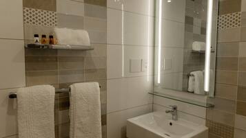 Un baño moderno con un estante de vidrio que contiene artículos de tocador, un lavabo blanco y un espejo grande.