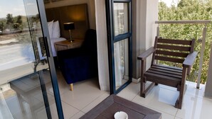 A balcony with a wooden bench, a small table with a cup, and a bed with a headboard and pillows. - Acres Inn Klerksdorp (Klerksdorp)