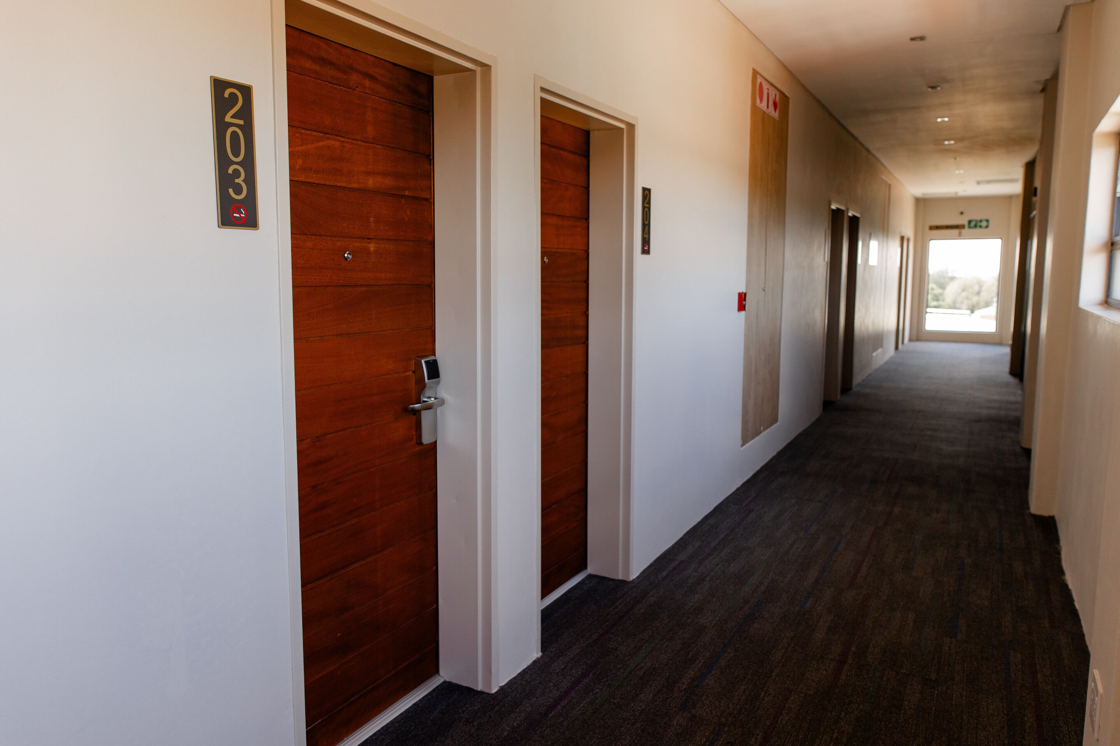 A hallway with wooden doors, numbered signs, and a carpeted floor.