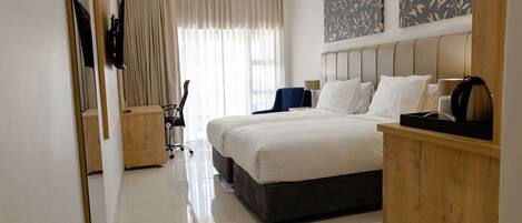 A hotel room with a large bed, a desk, a chair, and a wardrobe.