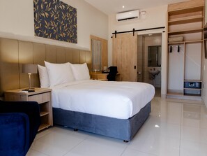 Ein modernes Hotelzimmer mit einem großen Bett, einem Schreibtisch, einem Stuhl, einem Kleiderschrank und einem sichtbaren Badezimmer durch eine offene Tür.