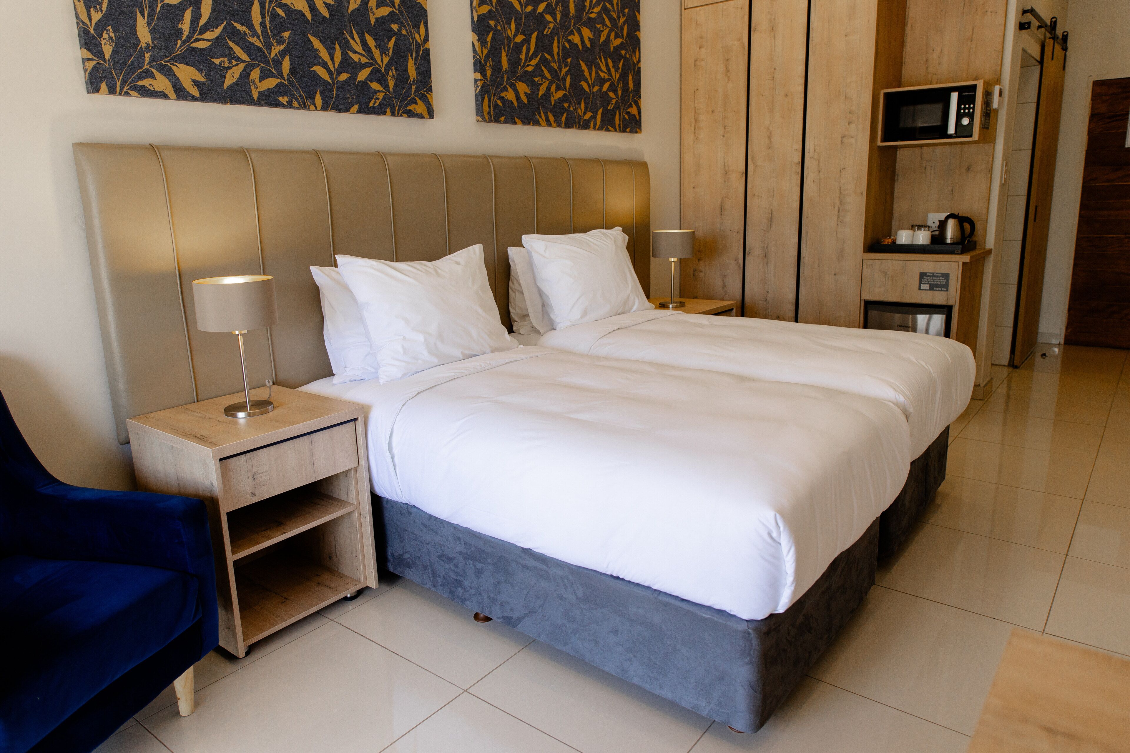A hotel room with a large bed, two bedside tables, a blue chair, a wooden cabinet, and a microwave.