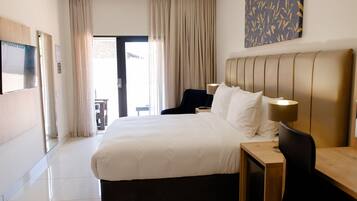 A hotel room with a large bed, a wooden headboard, two bedside lamps, and a view of the outdoors through a door.