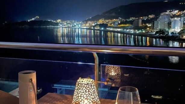 Une table avec un verre à vin et une lampe, donnant sur une vue nocturne de la ville.