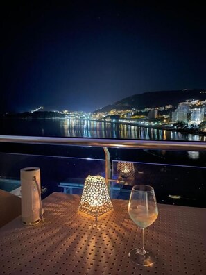 Une table avec un verre à vin et une lampe, donnant sur une vue nocturne de la ville.