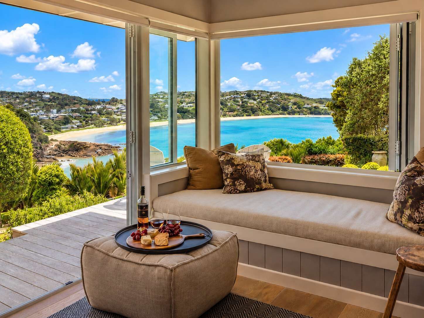 A room with a large window overlooking a beach, a cushioned seating area, and a tray with food and drink.