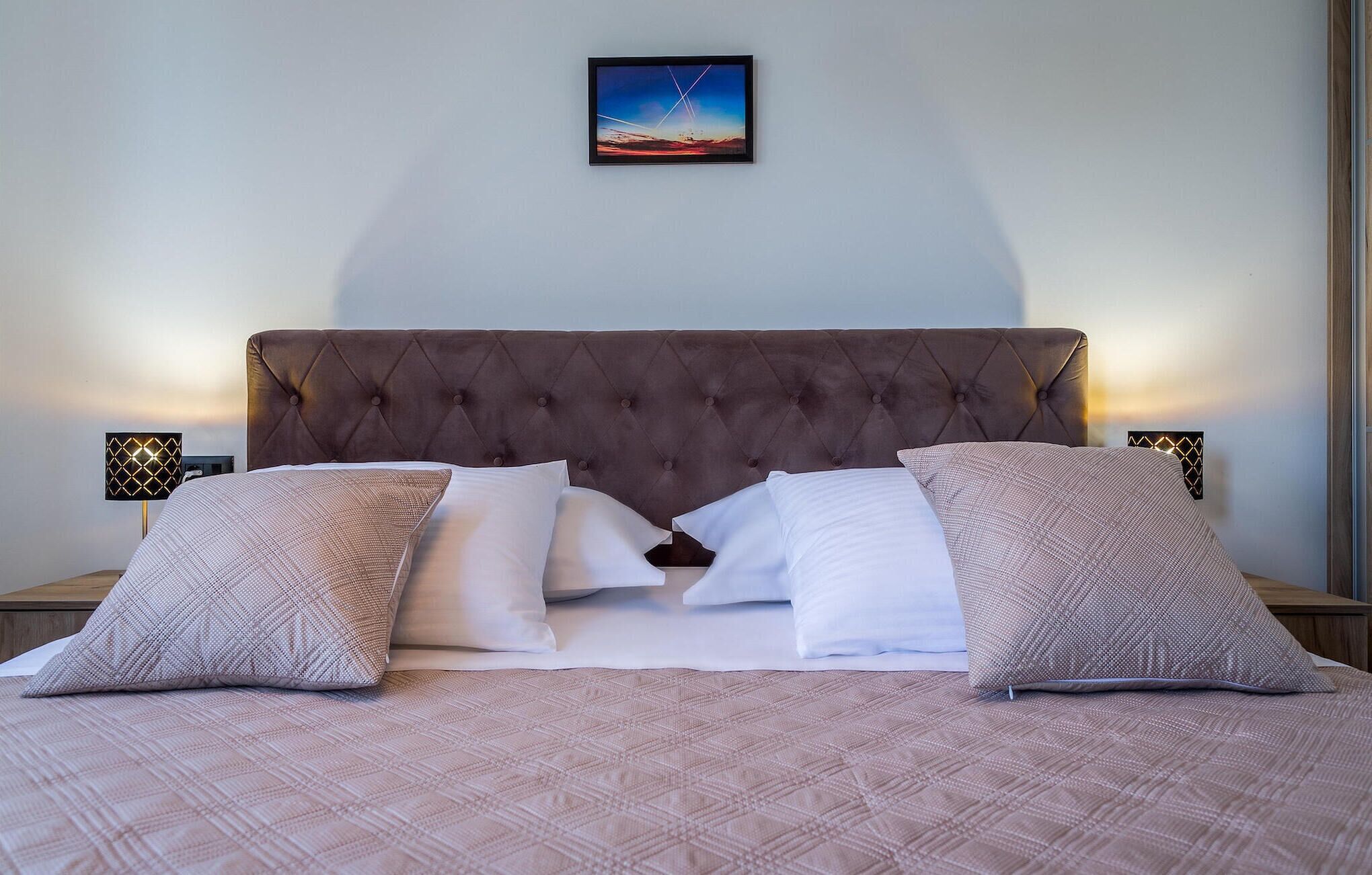 Ein ordentlich bezogenes Bett mit einer gesteppten Kopfteil, zwei Nachttische mit Lampen und ein gerahmtes Bild an der Wand.
