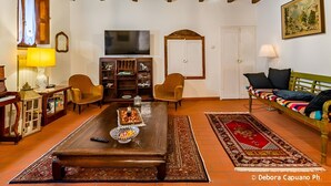 Una sala de estar acogedora con una mesa de centro de madera, dos sillones, un sofá, un televisor y una estantería.