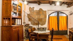 Un comedor con una mesa y sillas de madera, un armario con puertas de cristal, una escalera y un amplio ventanal con cortinas naranjas.