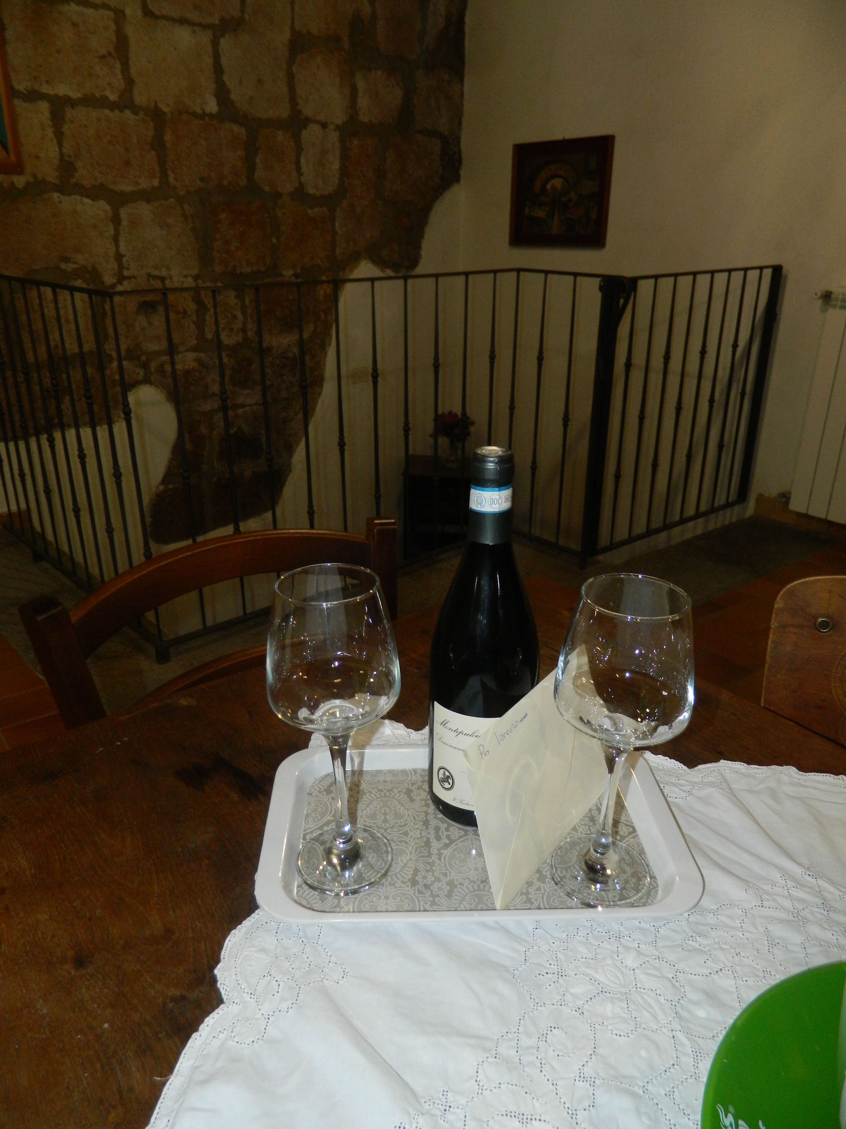A table with two wine glasses and a bottle of wine, set on a lace tablecloth.